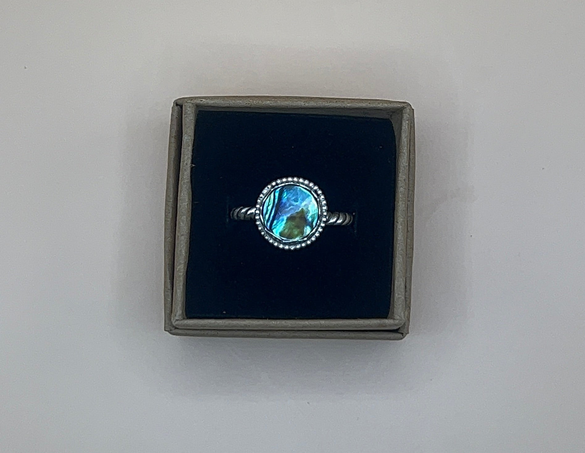 Ring with abalone shell in a black box on a light gray background